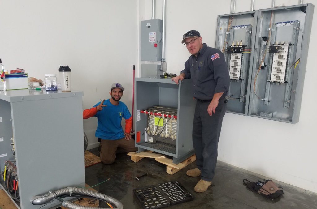 two electricians standing next to electrical panels